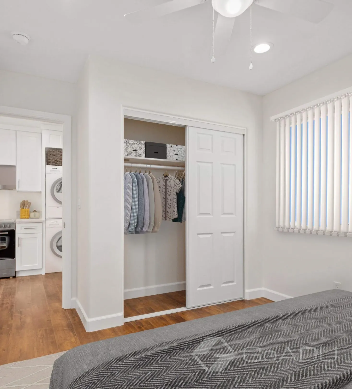 Custom adu bedroom with closet, ceiling fan, and view of kitchen with laundry area.