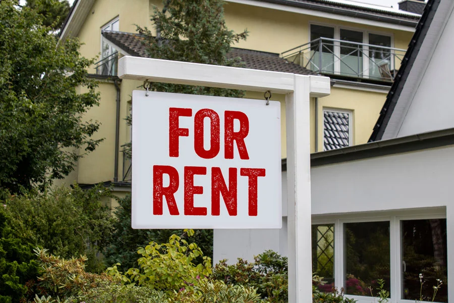 Wooden sign in front of a house with the message for rent